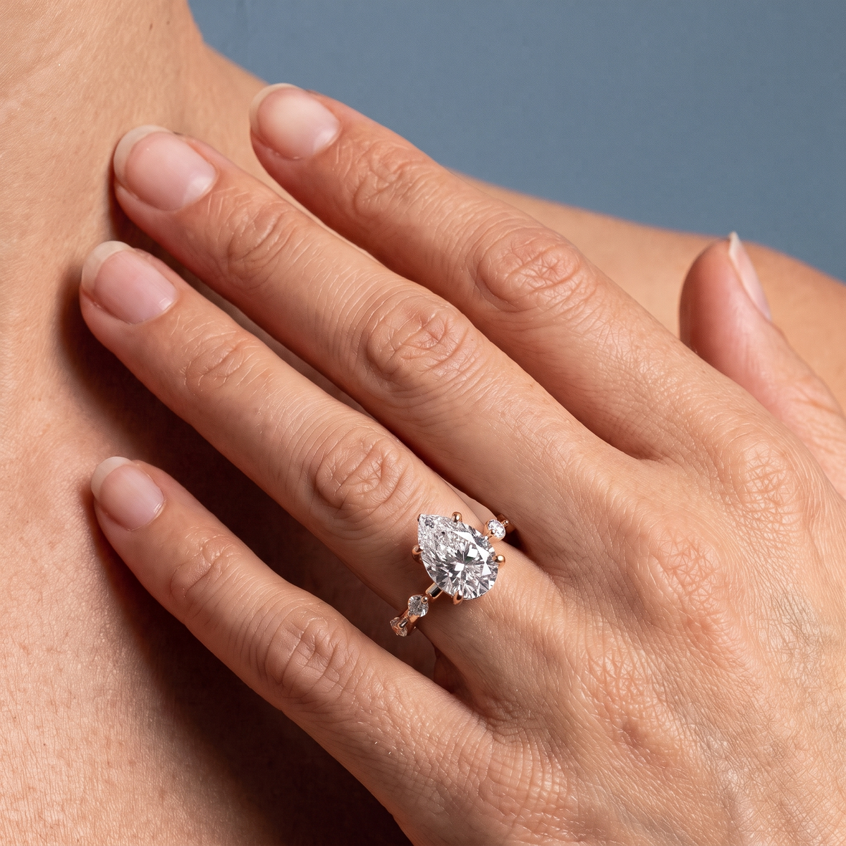 18 KT Rose Gold Pear Cut Diamond Solitaire Ring with Floating Diamond Accents - worn close-up